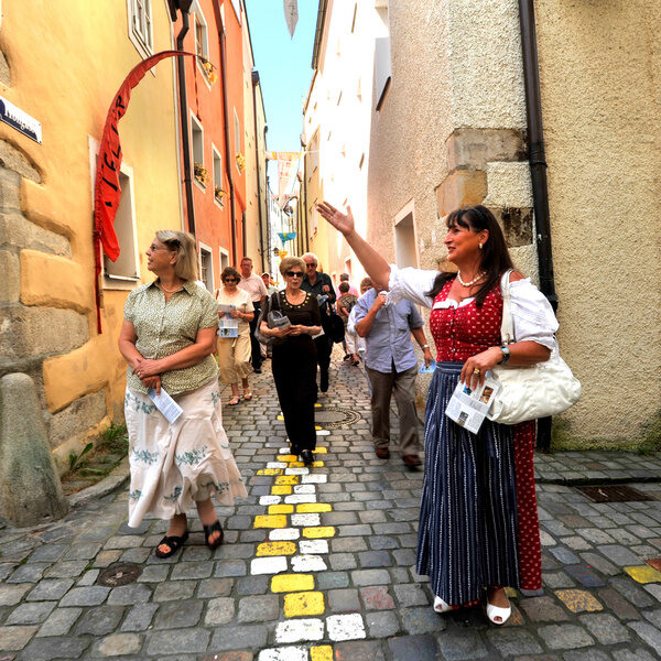 Eine Gruppe von Menschen spaziert durch die bunte Kopfsteinpflasterstraße in Passaus Altstadt.